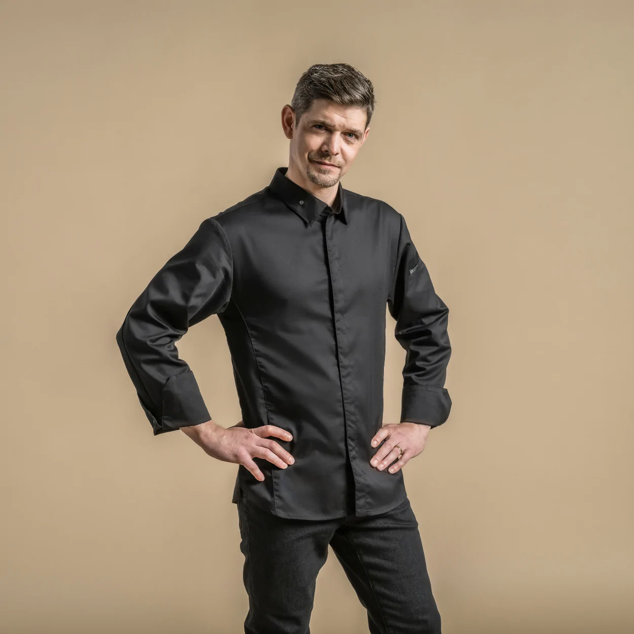 Unisex musta kokkitakki, jossa teräksiset napit kauluksessa ja hihansuissa.